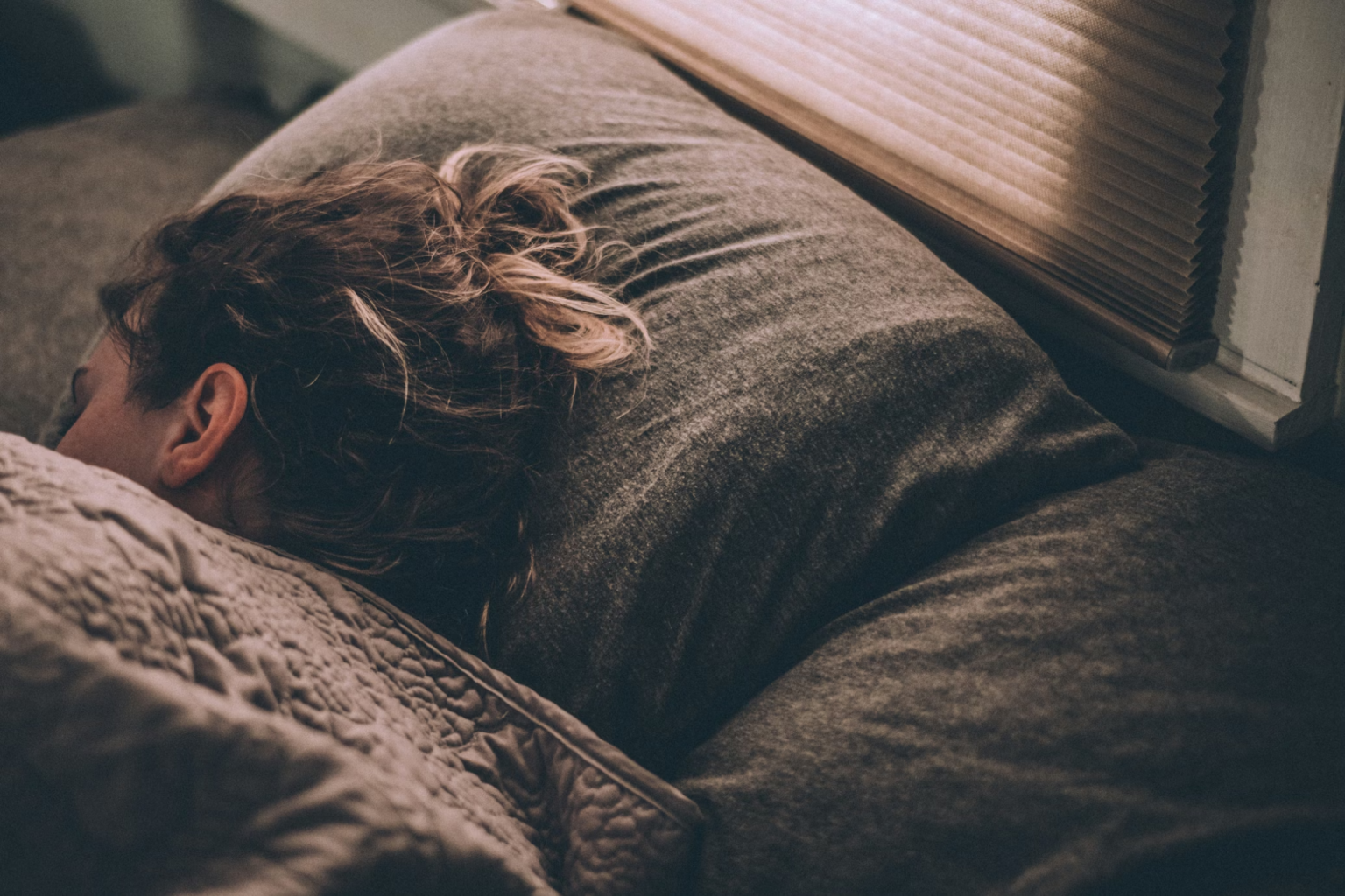 woman sleeping under blankets in a soft, natural light bedroom setting