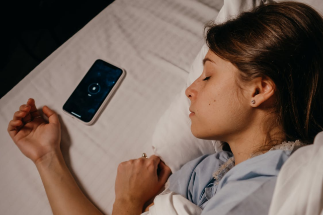 Participant sleeping beside a smartphone used to record event markers and contextual information during a longitudinal monitoring study.