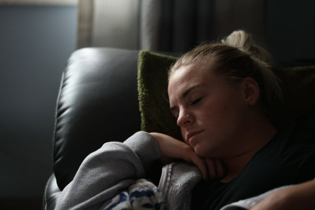 Person resting on a couch with eyes closed during fatigue recovery or sleep-related observation